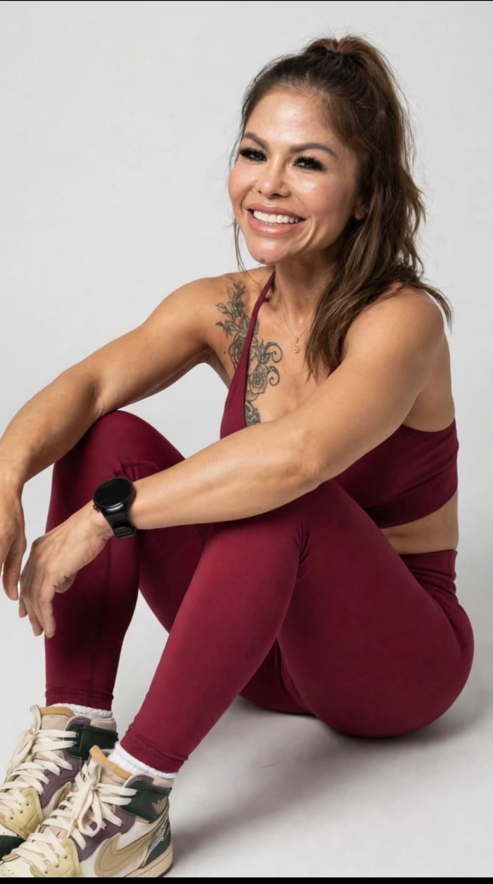 Jasmin smiling, sitting on the floor in burgundy activewear